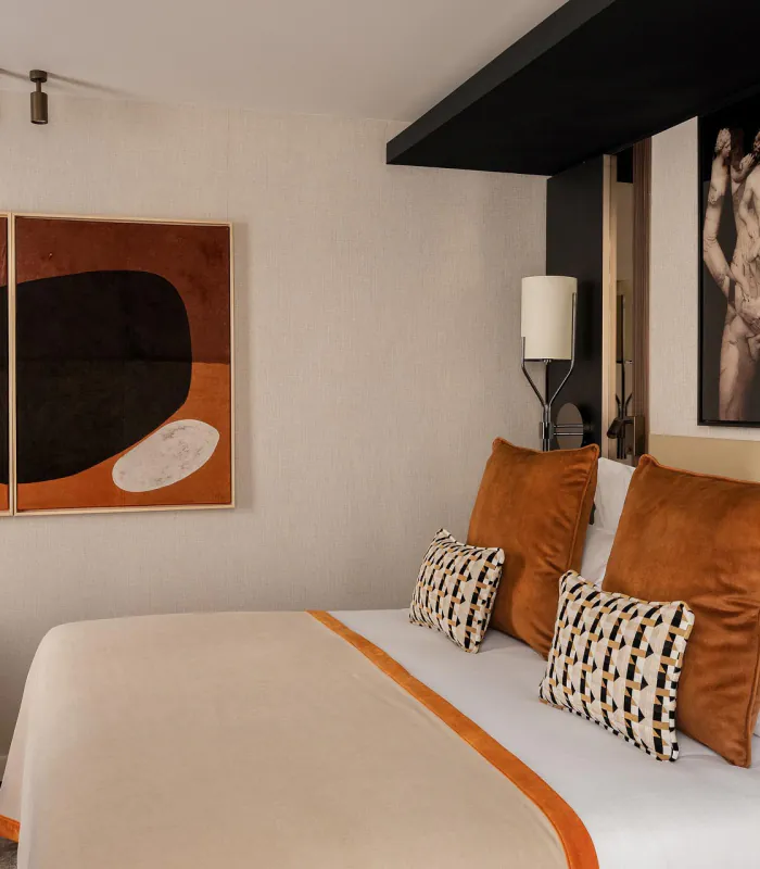 Chambre Classique de l’Hôtel Barnett à Paris avec lit double, coussins terracotta et œuvres d’art contemporaines.