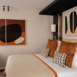 Chambre Supérieure de l’Hôtel Barnett à Paris avec lit double, coussins terracotta, fauteuil et œuvres d’art contemporaines.