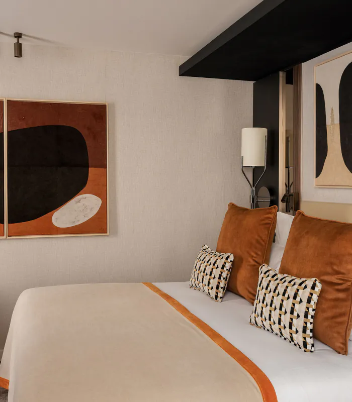 Chambre Supérieure de l’Hôtel Barnett à Paris avec lit double, coussins terracotta, fauteuil et œuvres d’art contemporaines.