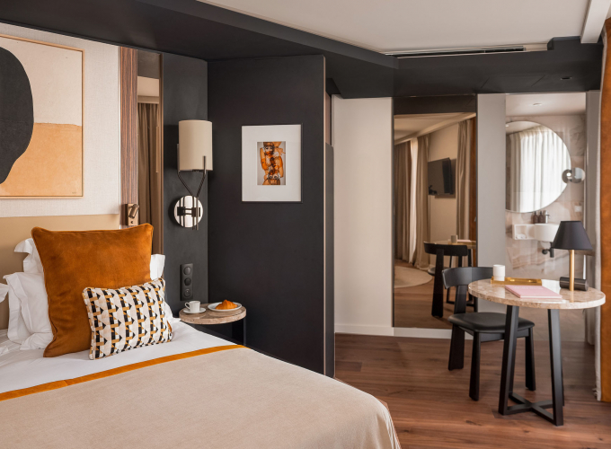 Chambre Supérieure de l’Hôtel Barnett à Paris avec lit double, coussins terracotta, fauteuil et œuvres d’art contemporaines.
