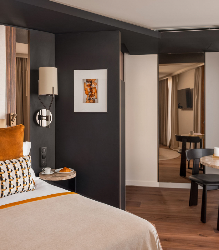 Chambre Supérieure de l’Hôtel Barnett à Paris avec lit double, coussins terracotta, fauteuil et œuvres d’art contemporaines.