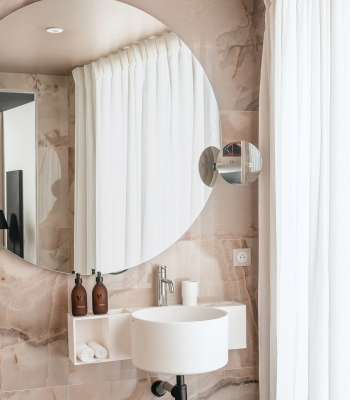 Salle de bains de la Chambre Classique de l’Hôtel Barnett à Paris avec vasque, miroir éclairé et revêtement en pierre naturelle.