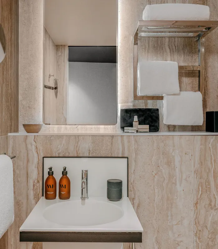 Salle de bains de la Chambre Classique de l’Hôtel Barnett à Paris avec vasque, miroir éclairé et revêtement en pierre naturelle.