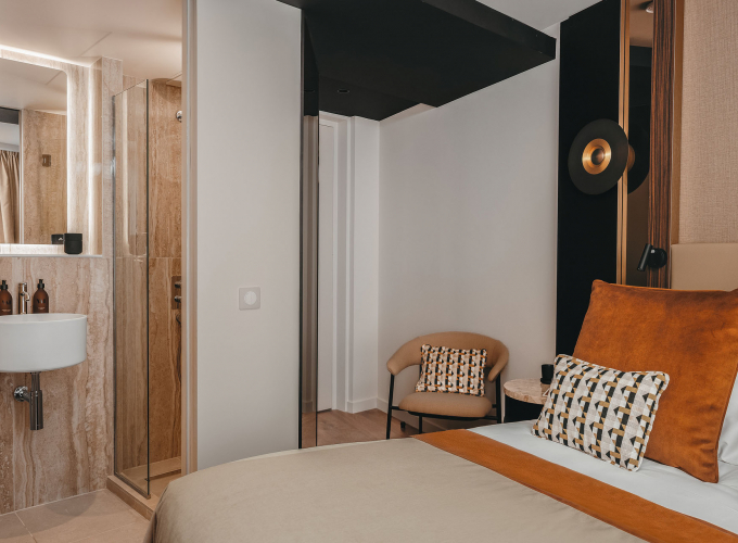 Chambre Cosy de l’Hôtel Barnett à Paris avec lit double, coussins terracotta et salle de bains ouverte en pierre.
