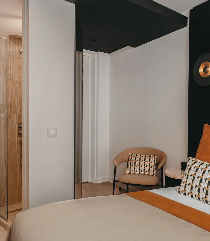 Chambre Cosy de l’Hôtel Barnett à Paris avec lit double, coussins terracotta et salle de bains ouverte en pierre.