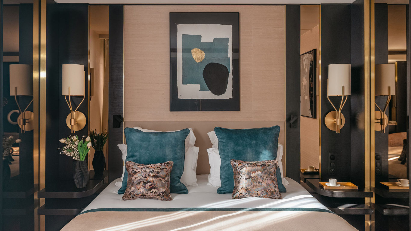 Chambre Supérieure de l’Hôtel Barnett à Paris avec lit double, coussins bleu canard, détails dorés et œuvre d’art contemporaine.