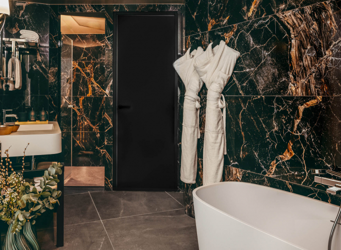 Salle de bains de la Chambre Prestige avec balcon de l’Hôtel Barnett à Paris avec baignoire îlot, marbre noir veiné et peignoirs.