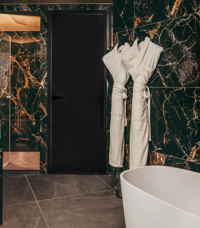 Salle de bains de la Chambre Prestige avec balcon de l’Hôtel Barnett à Paris avec baignoire îlot, marbre noir veiné et peignoirs.