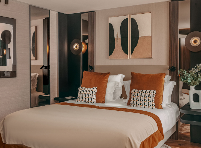 Chambre Deluxe de l’Hôtel Barnett à Paris avec lit double, coussins terracotta, miroirs et œuvres d’art contemporaines.
