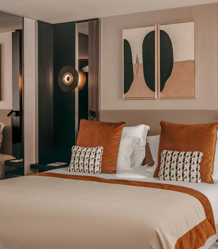 Chambre Deluxe de l’Hôtel Barnett à Paris avec lit double, coussins terracotta, miroirs et œuvres d’art contemporaines.