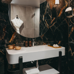 Salle de bains de la Chambre Deluxe de l’Hôtel Barnett à Paris avec marbre noir veiné, vasque blanche, miroir rond et douche.
