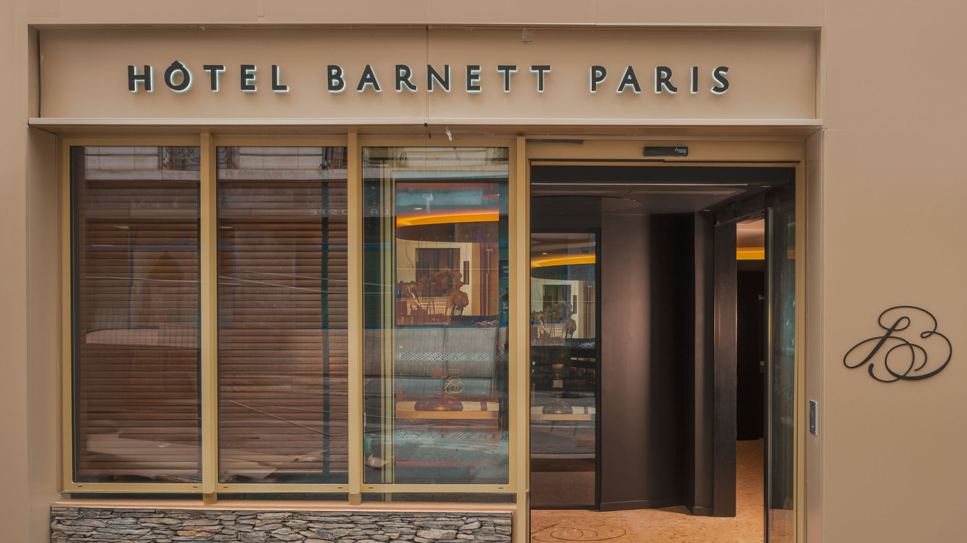 Façade de l’Hôtel Barnett à Paris avec entrée vitrée et enseigne lumineuse Hôtel Barnett Paris.