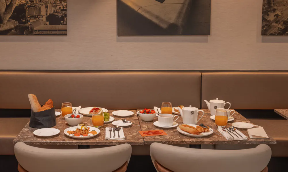 Table de petit-déjeuner de l’Hôtel Barnett à Paris avec viennoiseries, fruits frais, jus et boissons chaudes.
