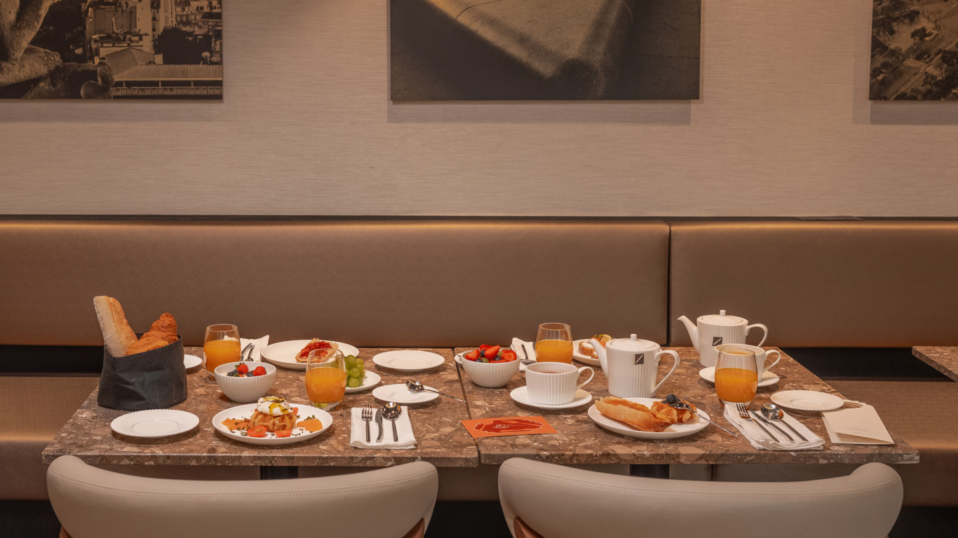 Table de petit-déjeuner de l’Hôtel Barnett à Paris avec viennoiseries, fruits frais, jus et boissons chaudes.