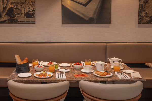 Table de petit-déjeuner de l’Hôtel Barnett à Paris avec viennoiseries, fruits frais, jus et boissons chaudes.