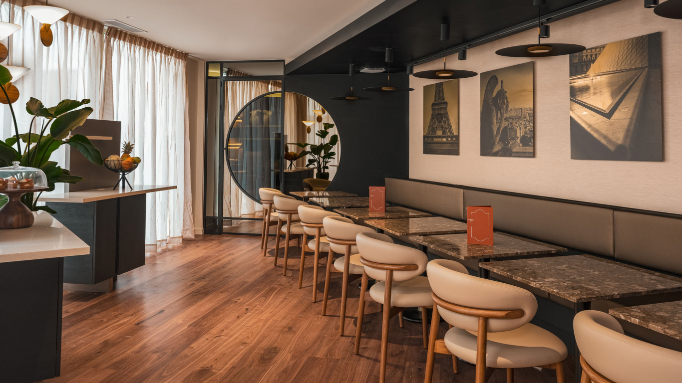 Salle de petit-déjeuner de l’Hôtel Barnett à Paris avec tables en pierre, fauteuils, photographies de Paris et grandes fenêtres.
