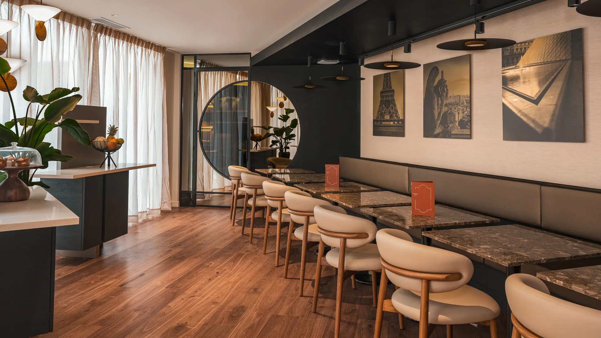 Salle de petit-déjeuner de l’Hôtel Barnett à Paris avec tables en pierre, fauteuils, photographies de Paris et grandes fenêtres.