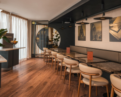 Salle de petit-déjeuner de l’Hôtel Barnett à Paris avec tables en pierre, fauteuils, photographies de Paris et grandes fenêtres.