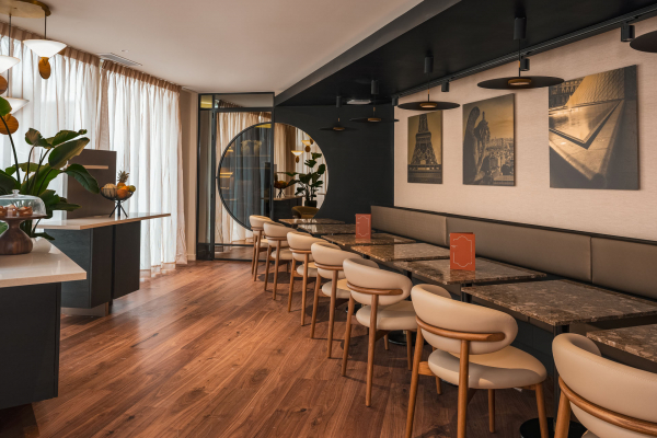 Salle de petit-déjeuner de l’Hôtel Barnett à Paris avec tables en pierre, fauteuils, photographies de Paris et grandes fenêtres.