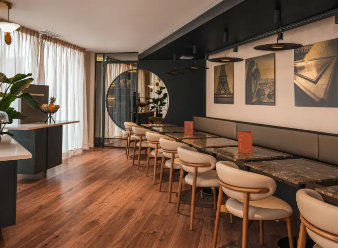 Salle de petit-déjeuner de l’Hôtel Barnett à Paris avec tables en pierre, fauteuils, photographies de Paris et grandes fenêtres.