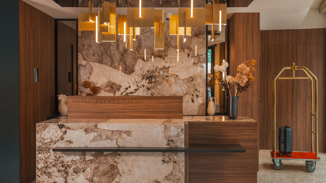 Réception de l’Hôtel Barnett à Paris avec comptoir en pierre et bois, luminaires dorés et décoration florale.