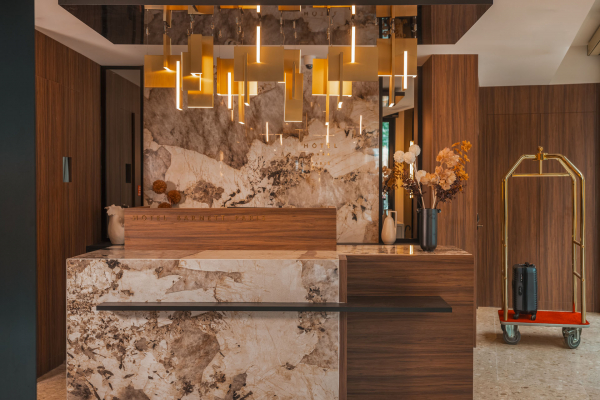 Réception de l’Hôtel Barnett à Paris avec comptoir en pierre et bois, luminaires dorés et décoration florale.
